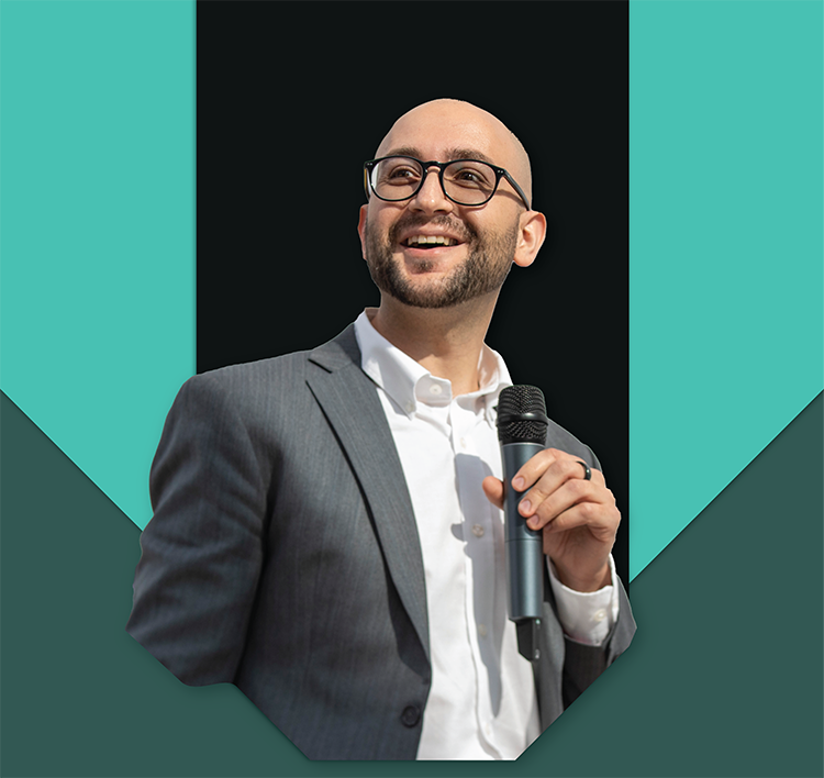 Wilhelm Klein holding a microphone and speaking at an event.