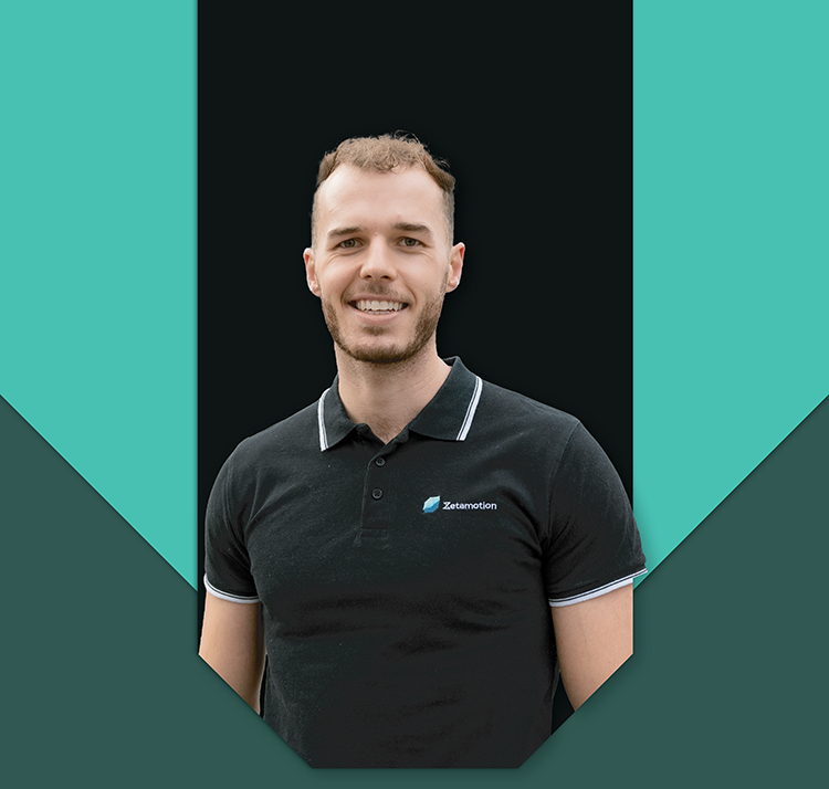 Michael Kurzewski, Sales and Creative Lead at Zetamotion, wearing a black Zetamotion polo shirt, smiling against a branded background.