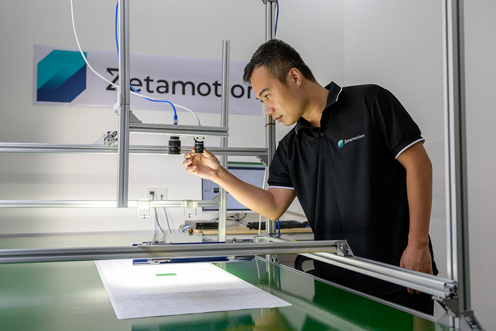 Technician inspecting a camera module on an AI-powered quality control machine at Zetamotion lab.